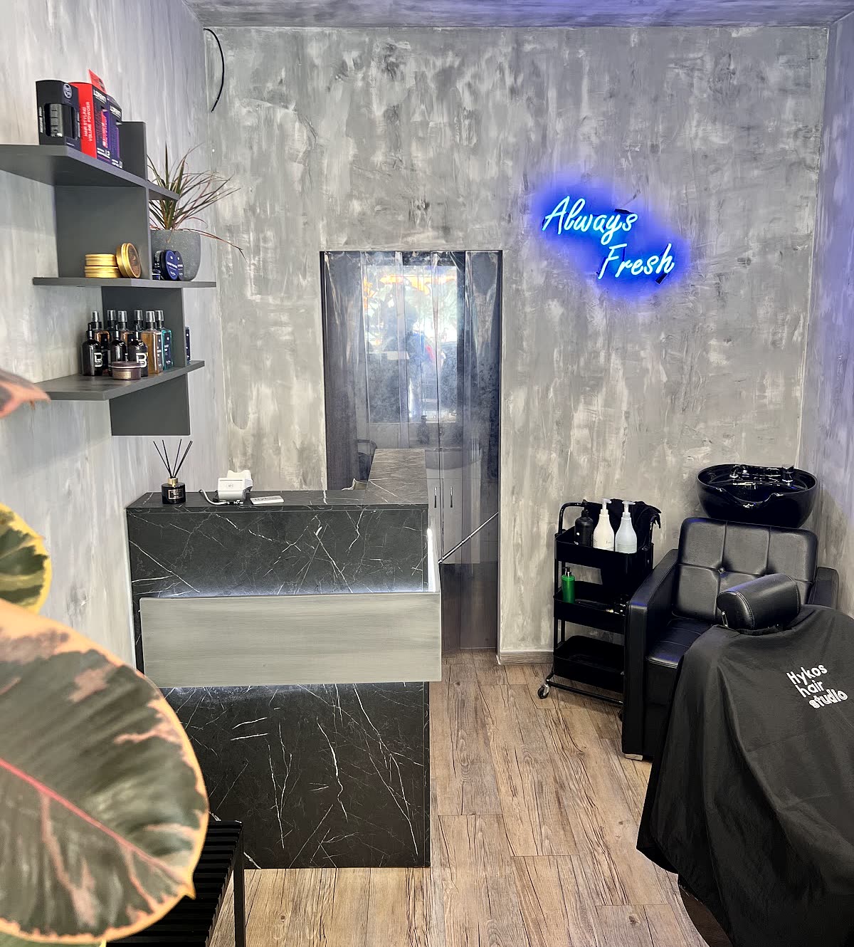 Το εσωτερικό του Hykos hair studio, ο τσιμεντένιος τοίχος με το μπλε νέον Always Fresh, ο πάγκος από μαύρο μάρμαρο και το ξύλινο πάτωμα
