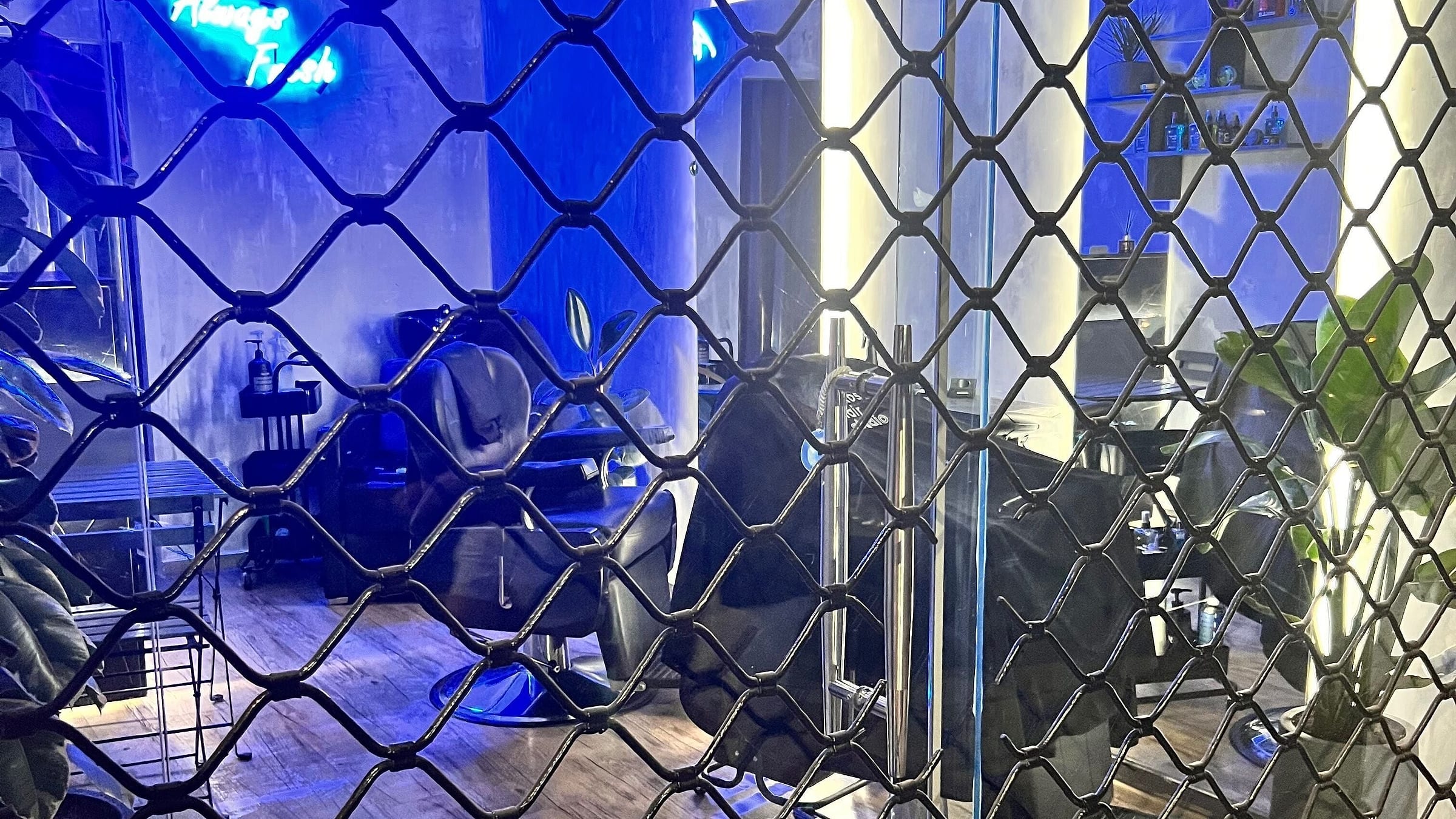Το Hykos hair studio τη νύχτα, μέσα από το κατεβασμένο ρολό, με το μπλε νέον αναμμένο