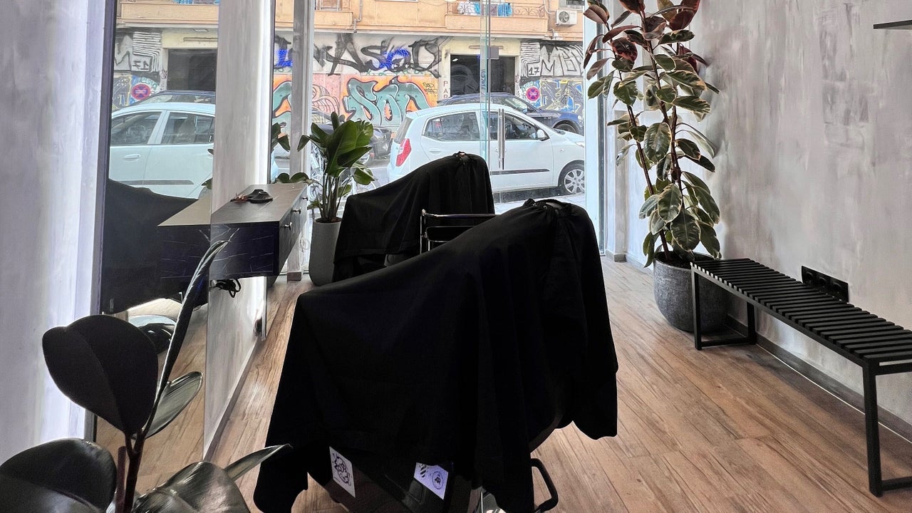 Οι δύο καρέκλες του Hykos hair studio με τις μαύρες κάπες τους, δίπλα στην τζαμαρία με θέα τον δρόμο